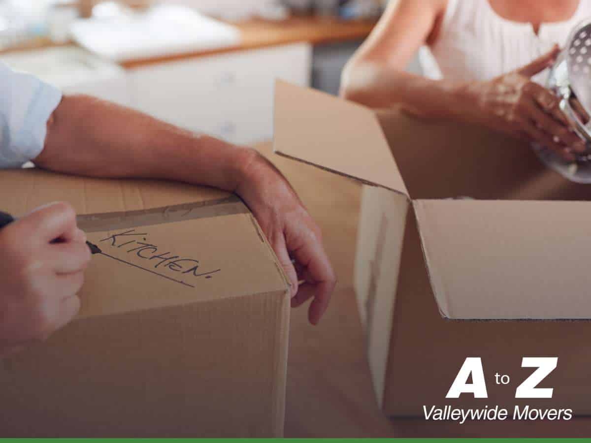 Person labeling a moving box for the kitchen, showing how to efficiently Pack a Kitchen For a Move